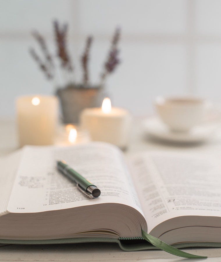 open book and pen next to lit candles