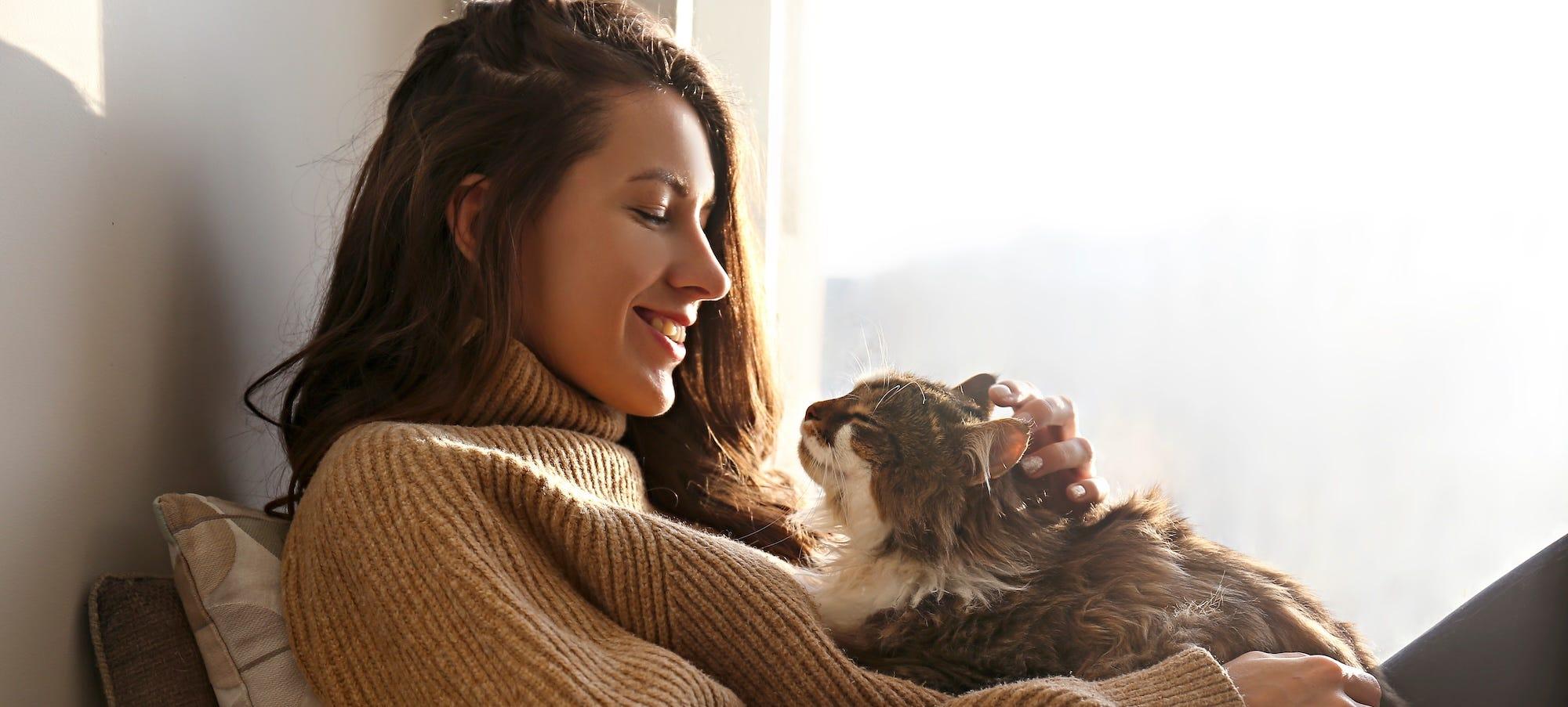woman smiling as she holds happy long-haired cat against her lap