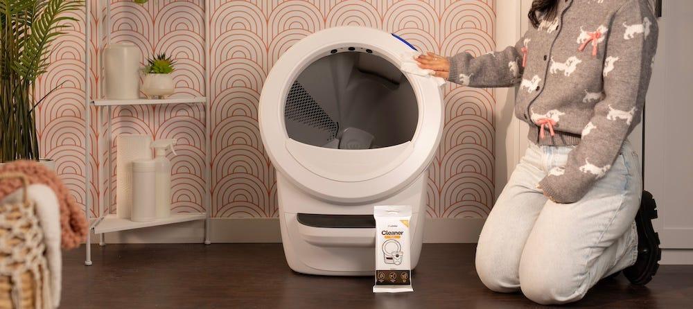 woman wiping down automatic litter box with cleaner