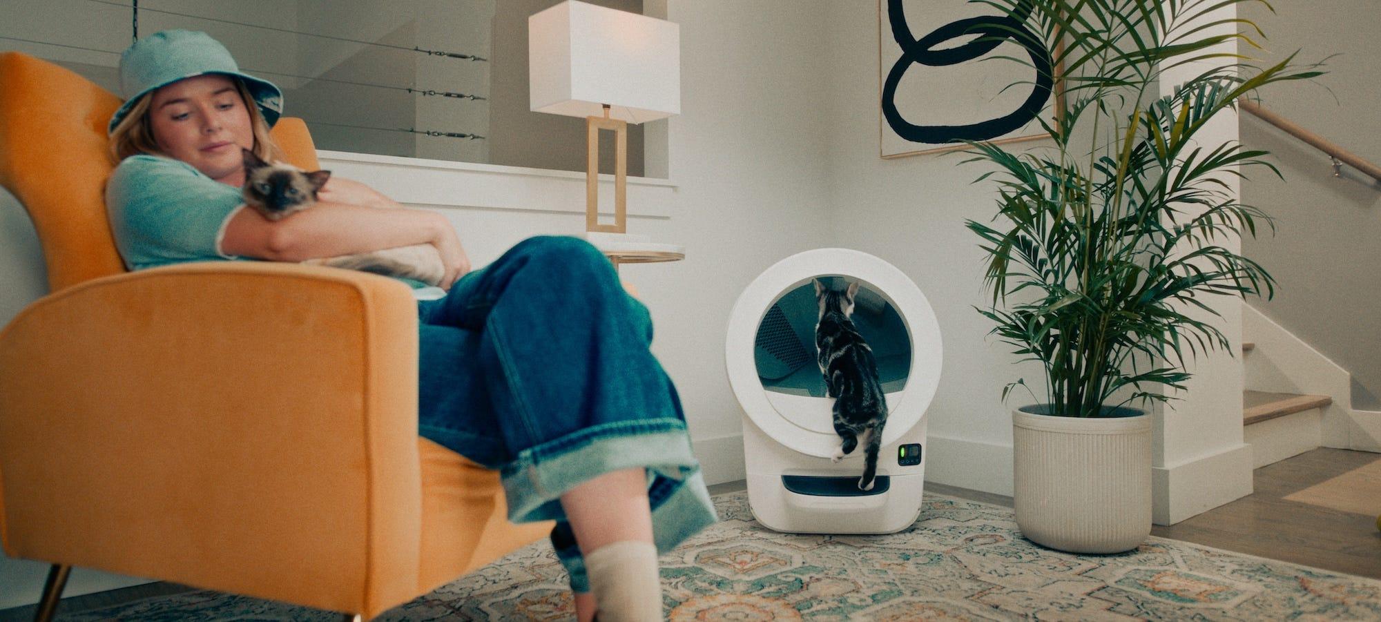 cat entering Litter-Robot while woman sits in chair holding cat