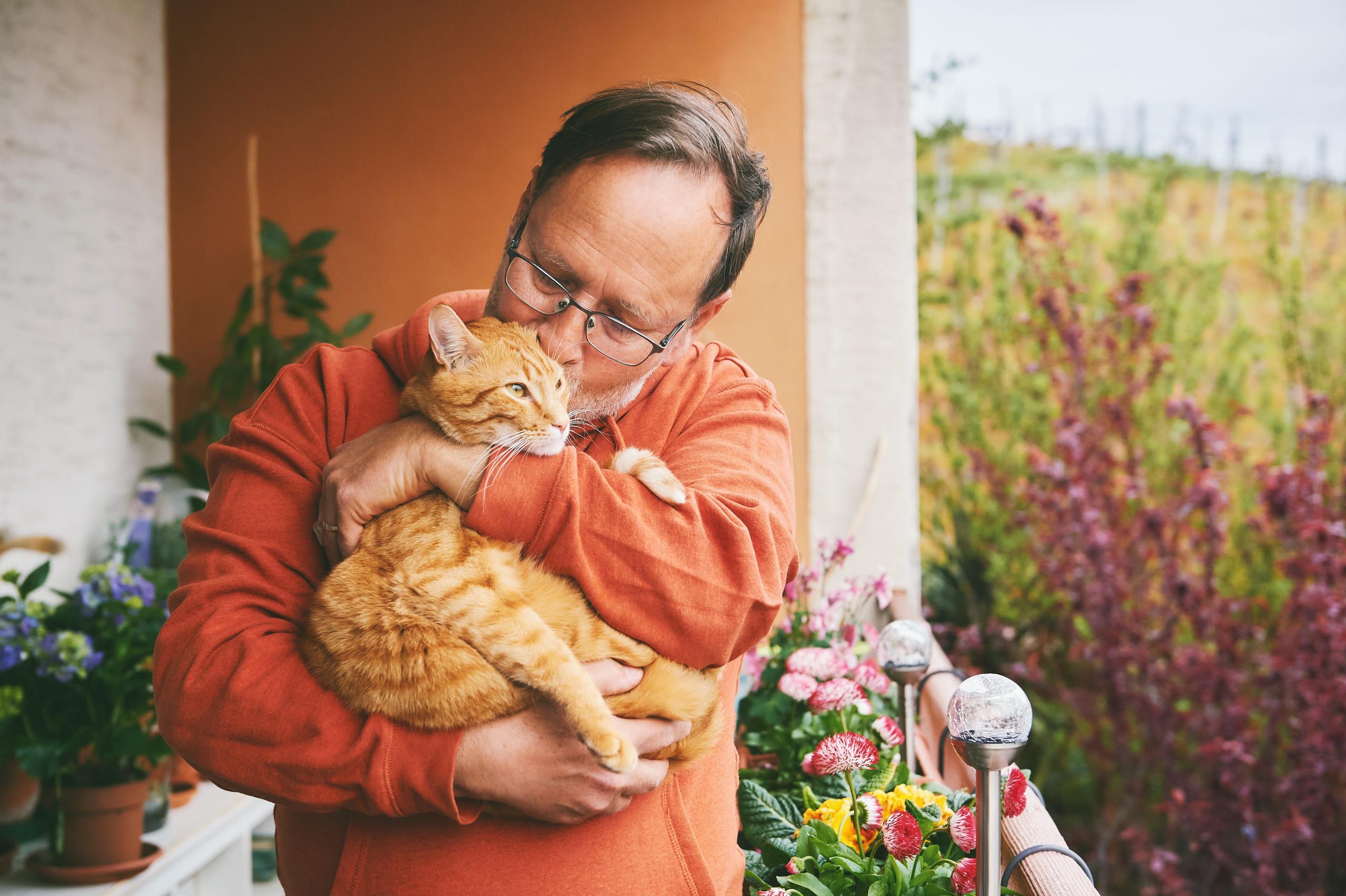 Man holding a cute ginger cat, resting on small cozy balcony