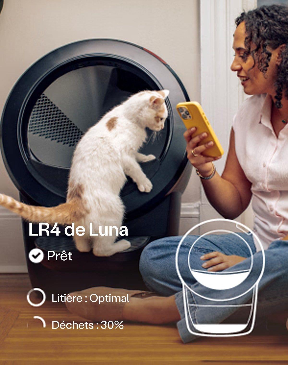 Woman sitting on floor checking the Litter-Robot 4 app on her phone while a white cat climbs into the Litter-Robot 4 with a status overlay showing 'Ready,' 'Litter: Optimal,' and 'Waste: 30% Full'
