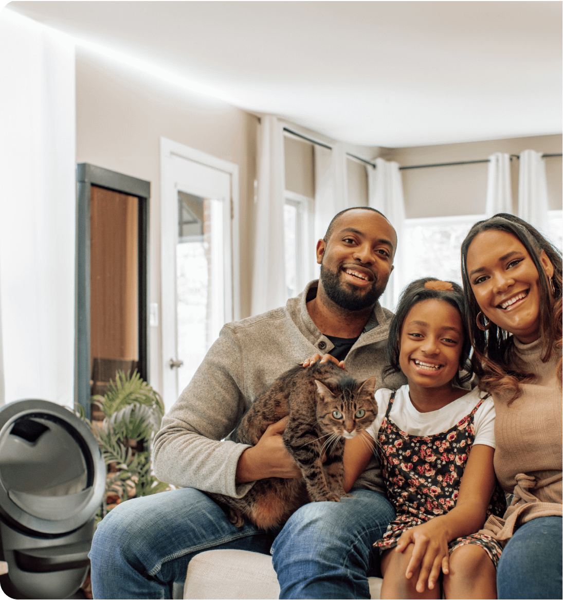 A family of 3 smiling and holding their cat wit ha Litter-Robot 4 in the background