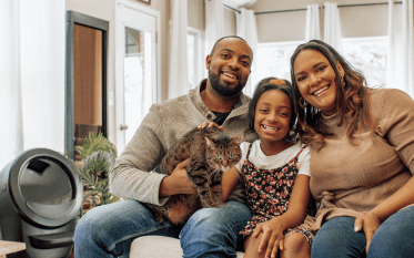 A family of 3 smiling and holding their cat wit ha Litter-Robot 4 in the background
