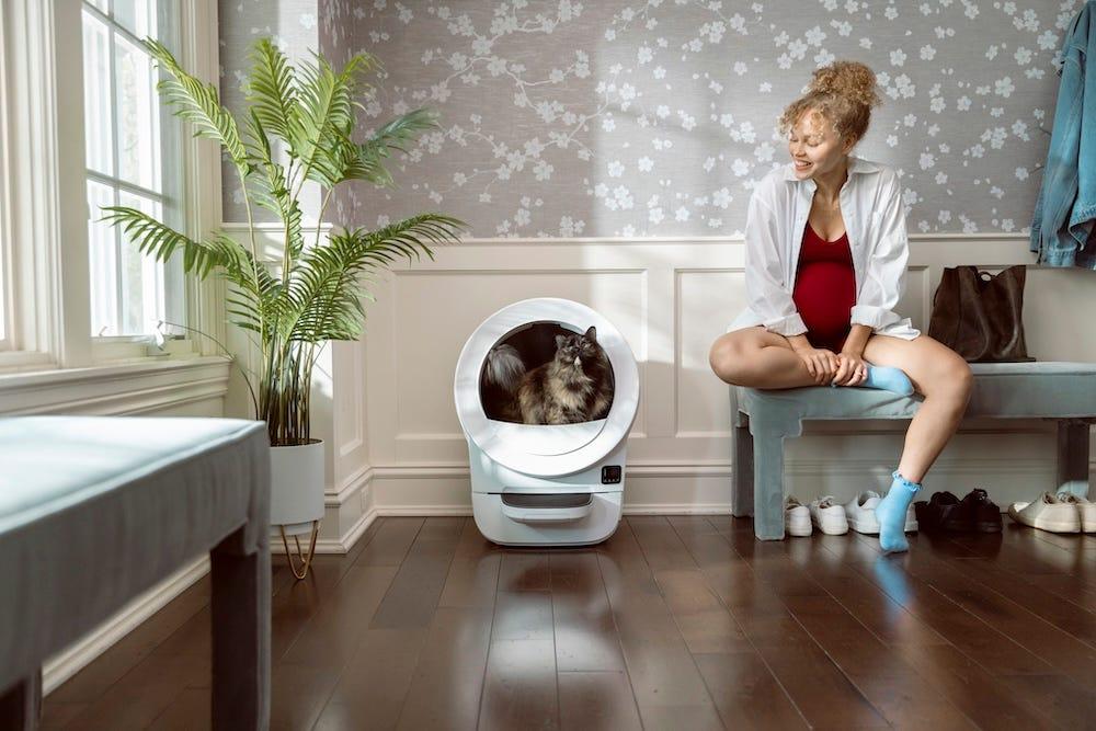 pregnant woman sitting near cat using self-cleaning litter box Litter-Robot EVO
