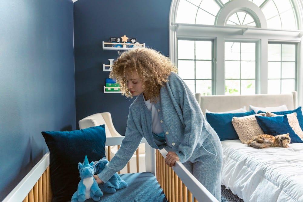 pregnant woman arranging baby nursery with cat on bed