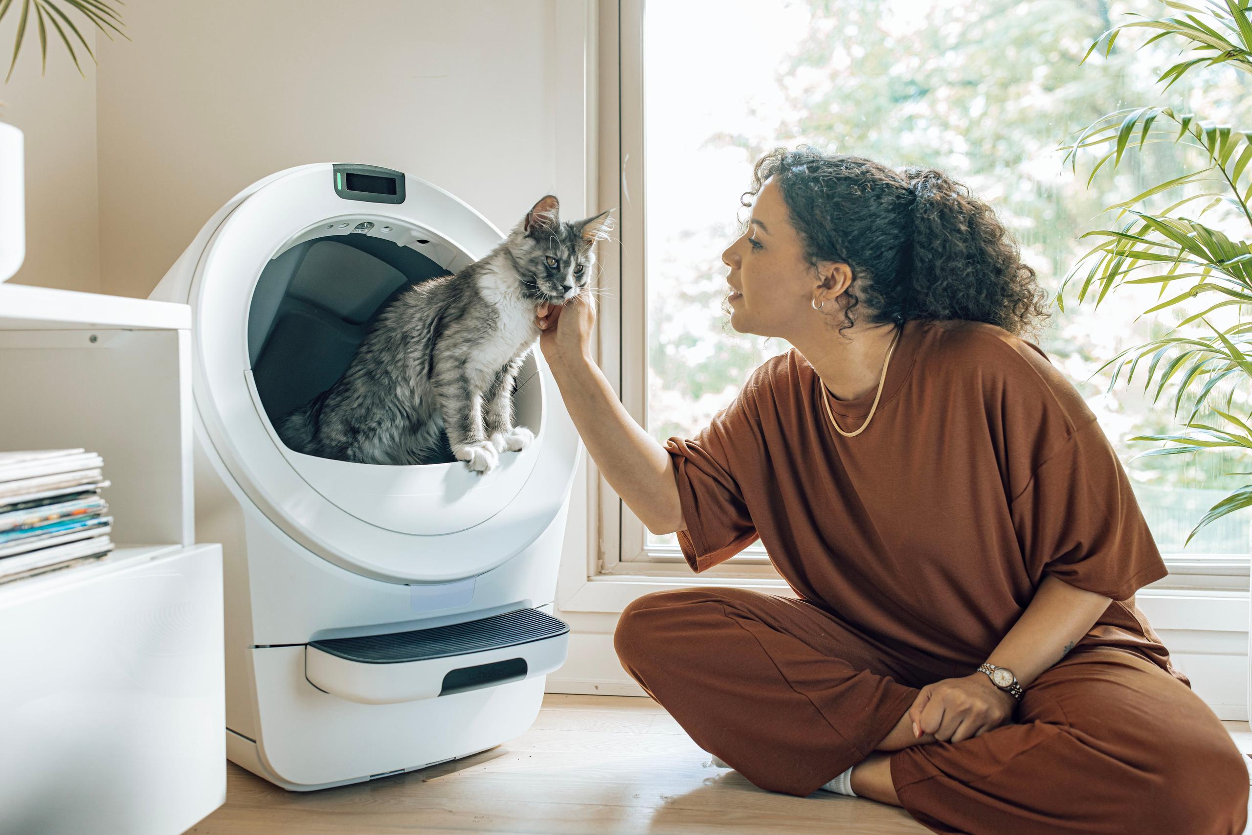 happy woman sitting next to self-cleaning litter box with cat