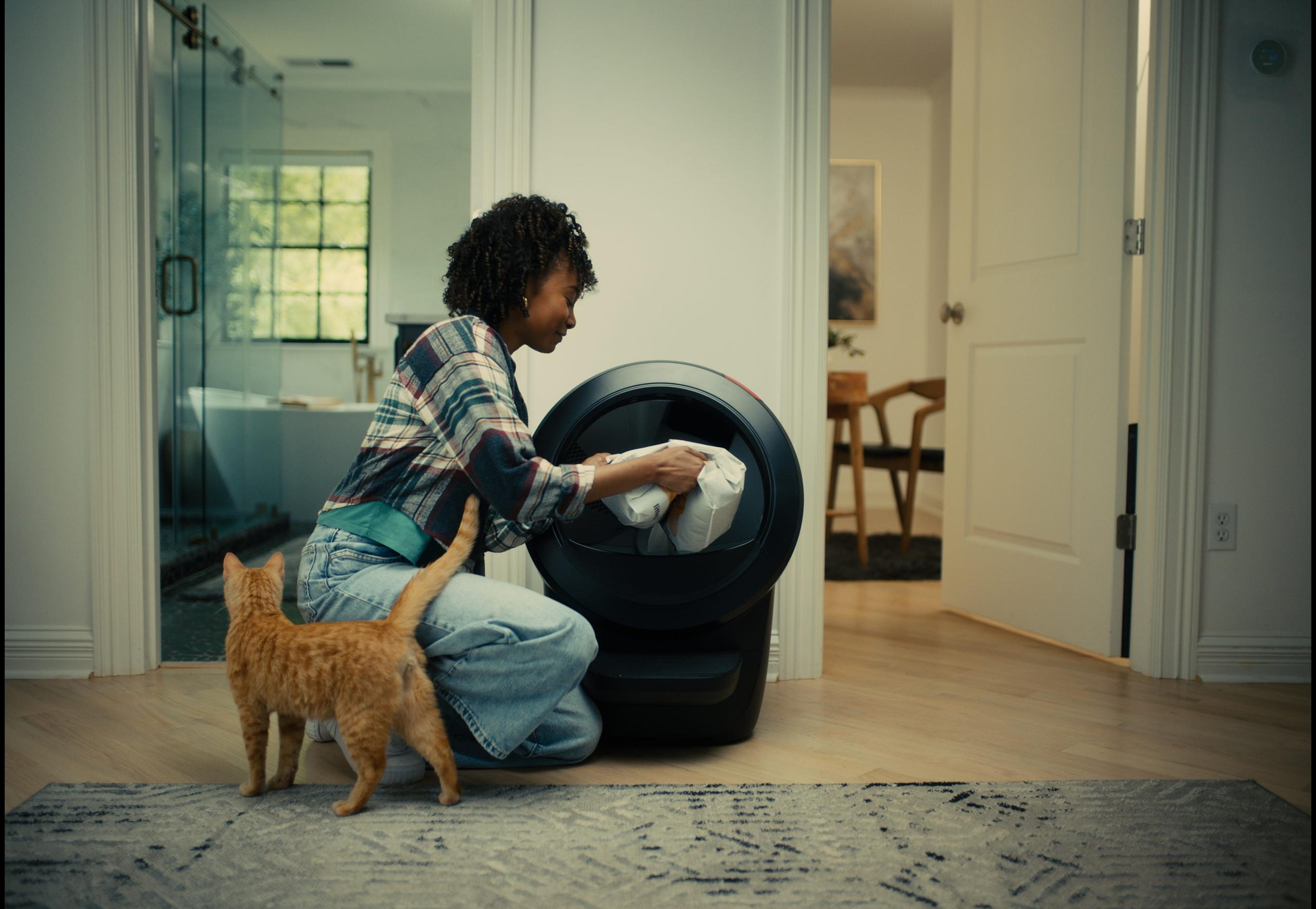 woman adding litter to Litter-Robot while orange tabby cat watches