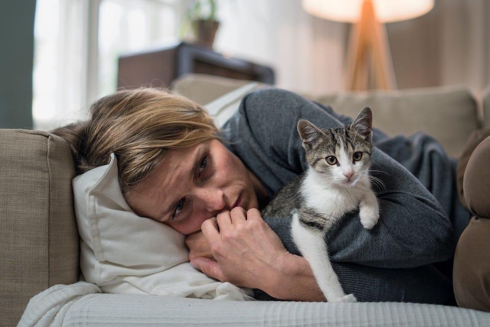 sad woman lying on couch holding cat for comfort
