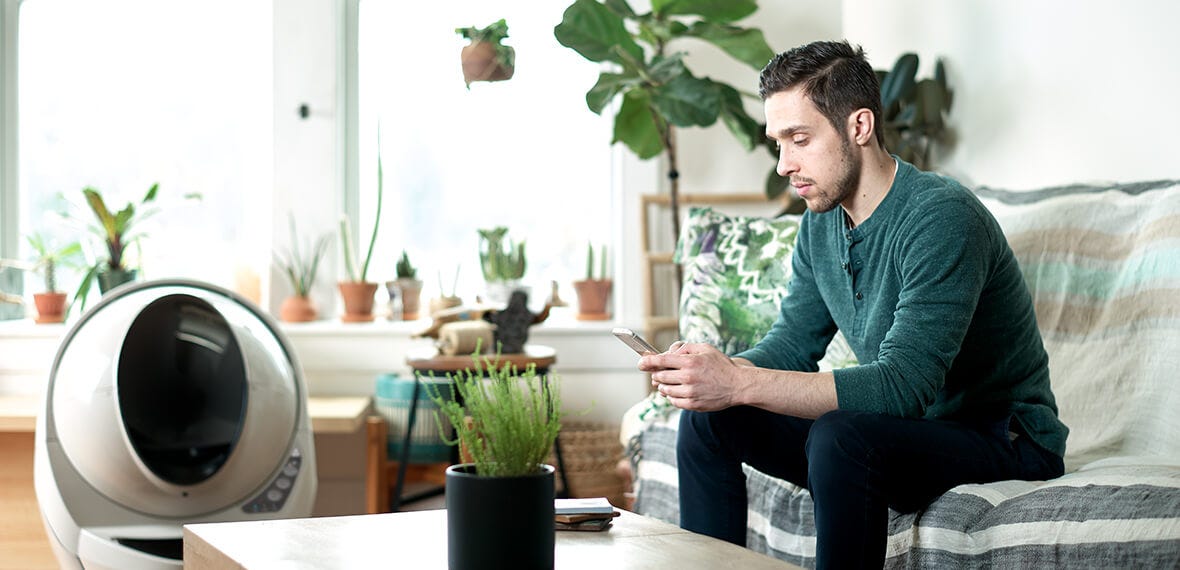Man looking at Litter-Robot 3 Connect app next to the robot litter