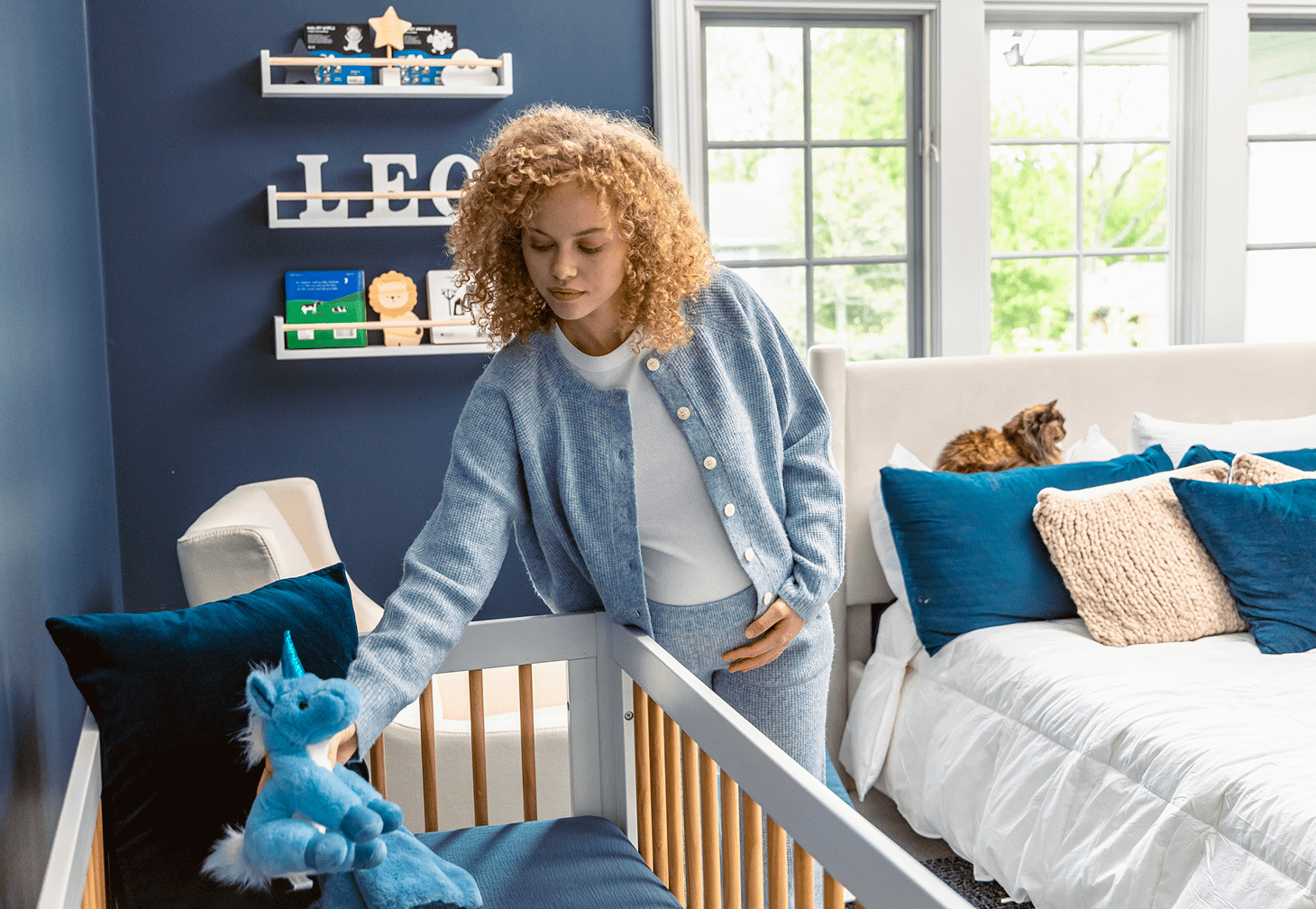 pregnant woman setting up nursery with cat on bed